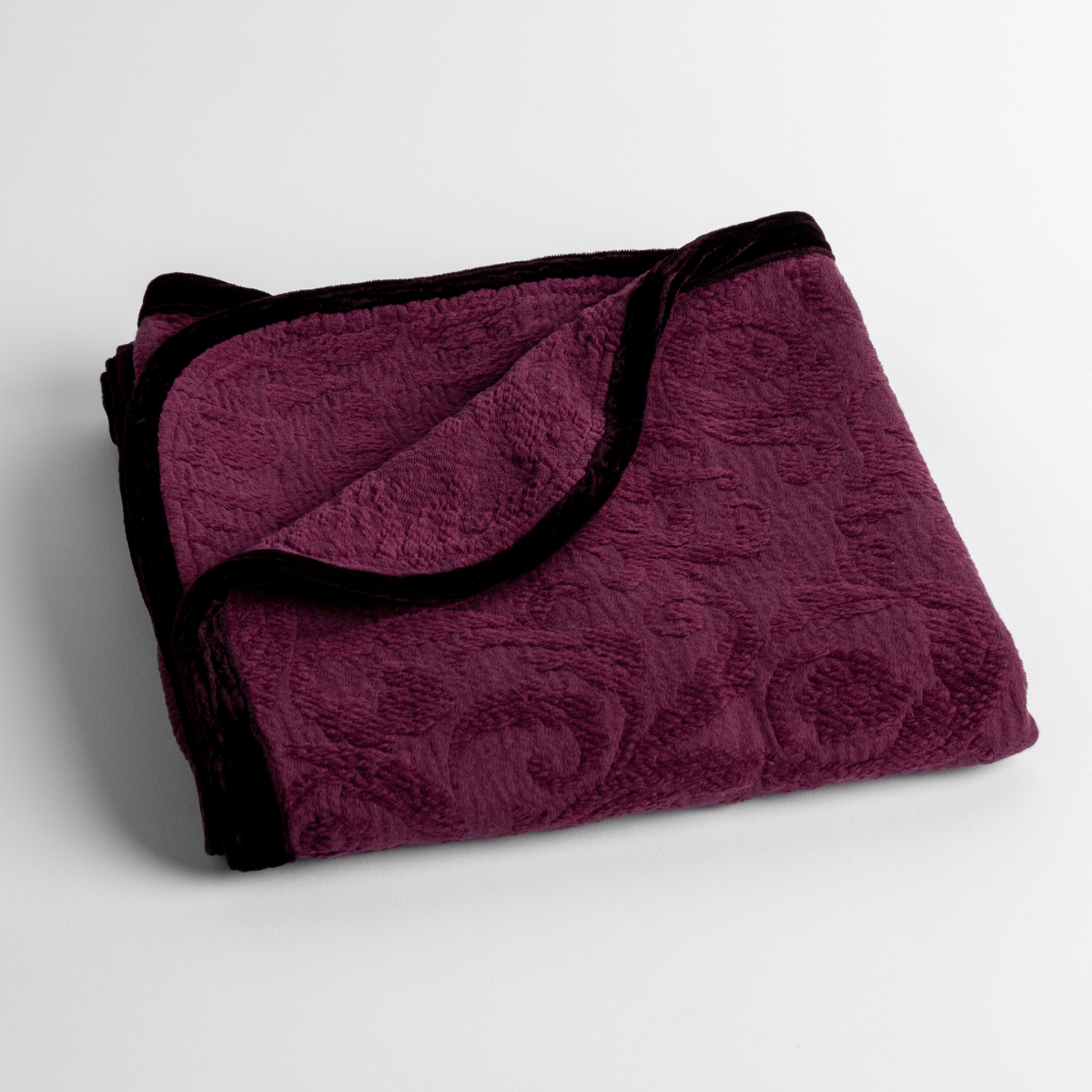 Fig: a folded blanket with the corner turned down to show the trim against a white background, shot from an overhead angle.