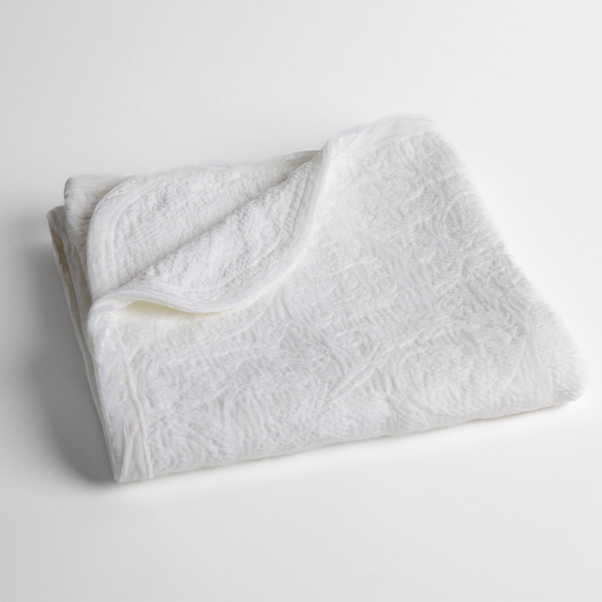 White: a folded blanket with the corner turned down to show the trim against a white background, shot from an overhead angle.