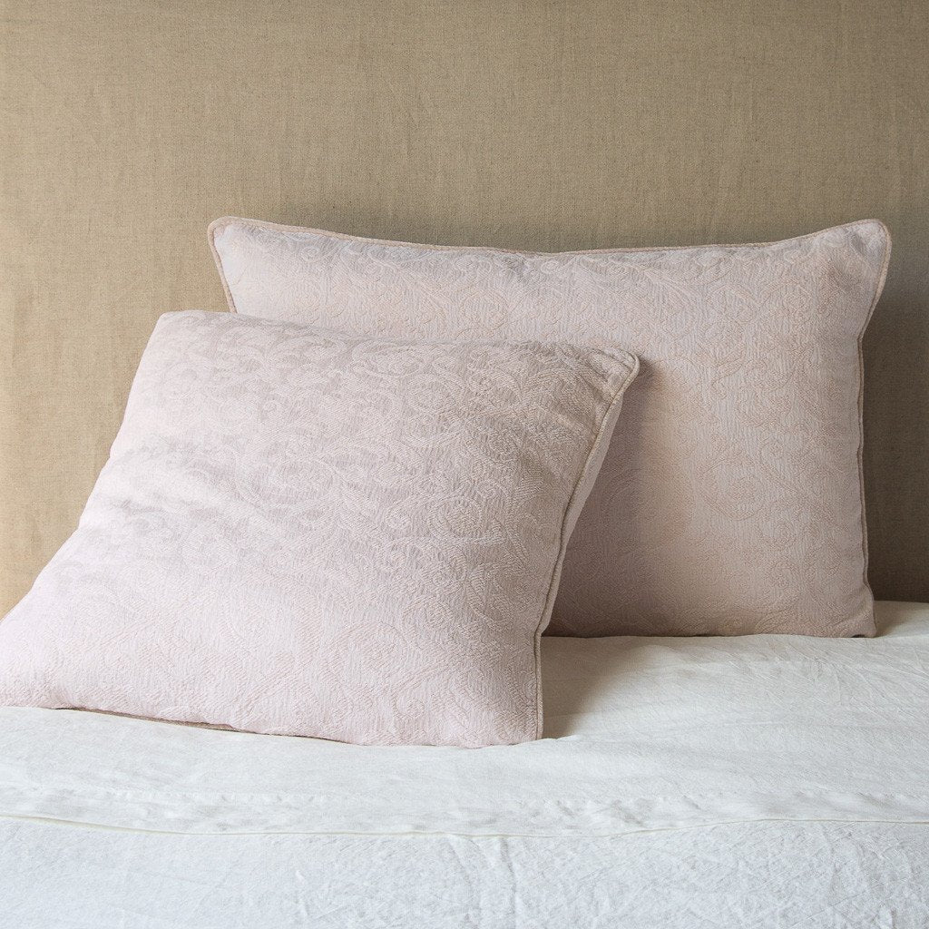 Pearl: Two Adele shams, shown in euro and deluxe sizes, leaning against a neutral toned headboard on white bedding.