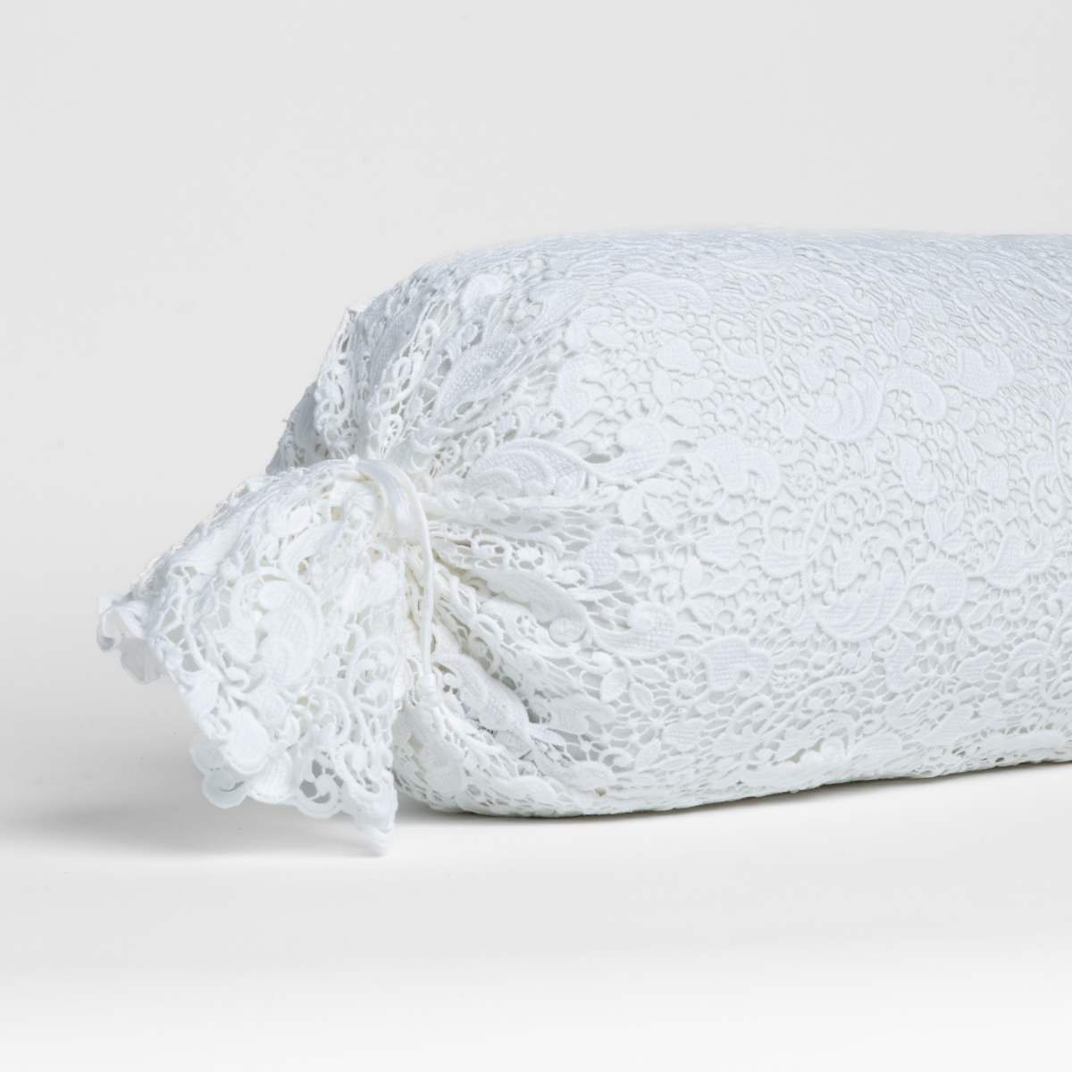 White: one end of a lace boslter cover on a winter white liner against a white background.
