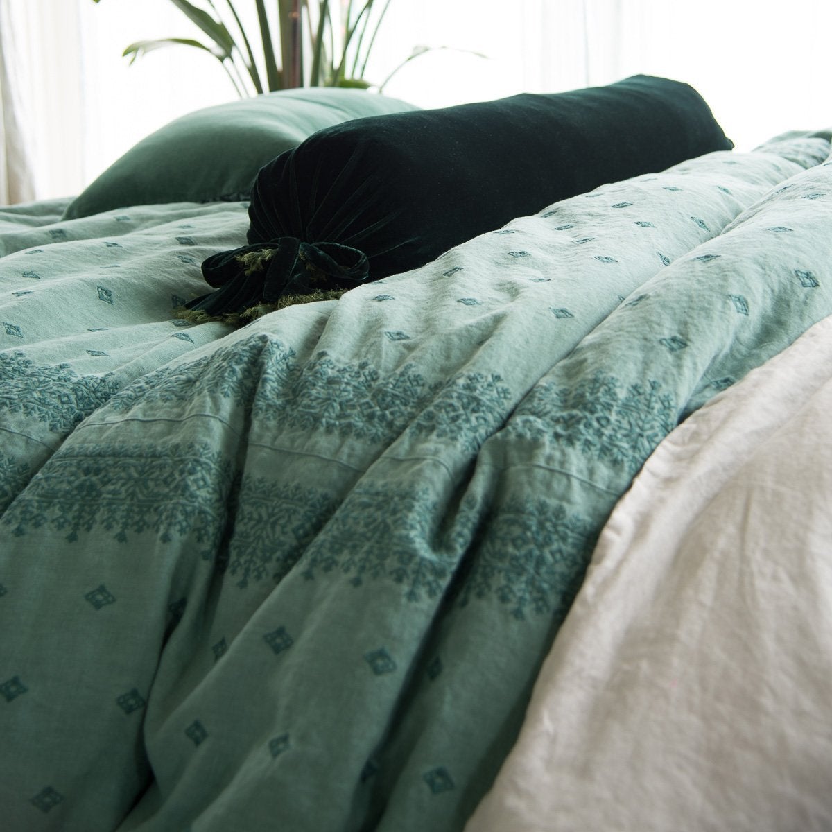 : Ines duvet cover in jade. The deeper tone of the cotton embroidery against the midweight linenshown is emphasized by a jade silk velvet bolster - close-up side view.