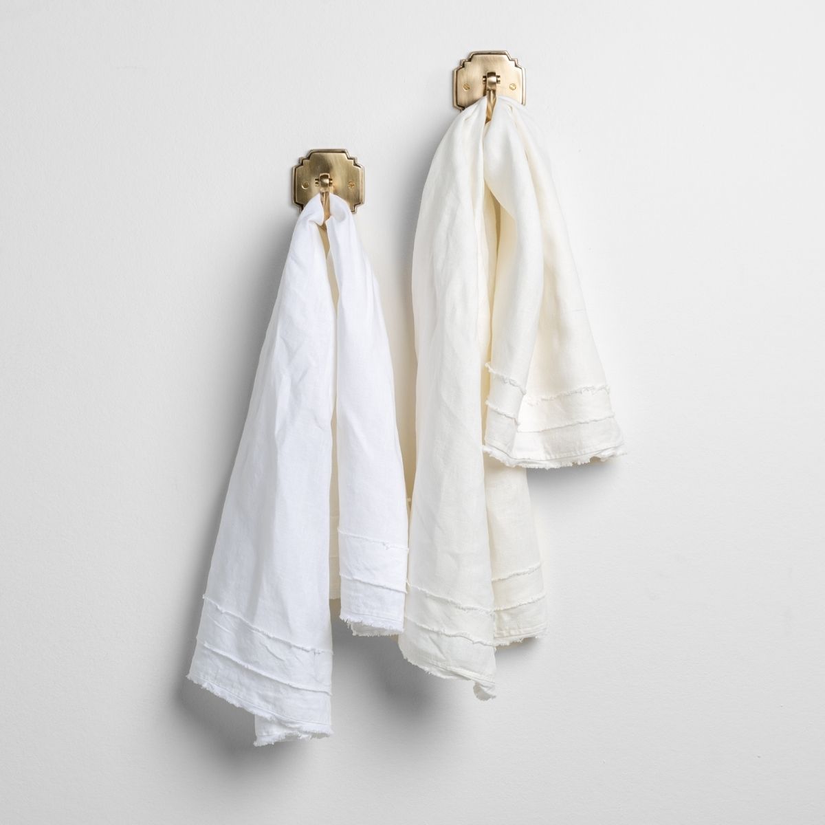 White: midweight linen guest towels in white and winter white on towel hooks mounted to a white wall.