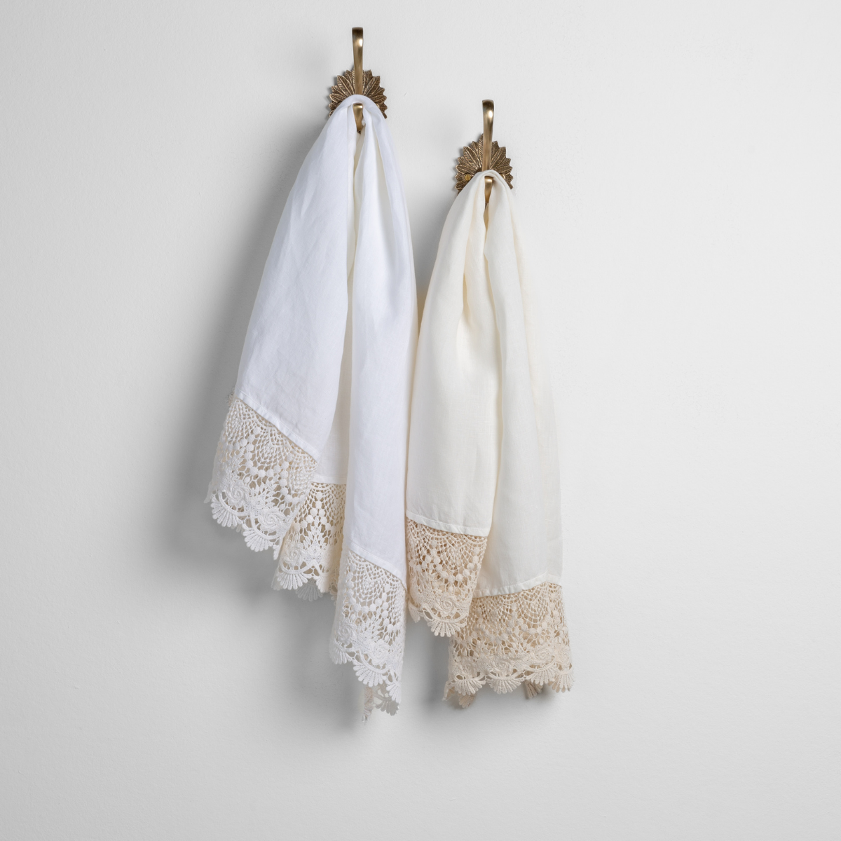 : two linen with lace guest towels in white and winter white on decorative towel hooks mounted on a white wall.