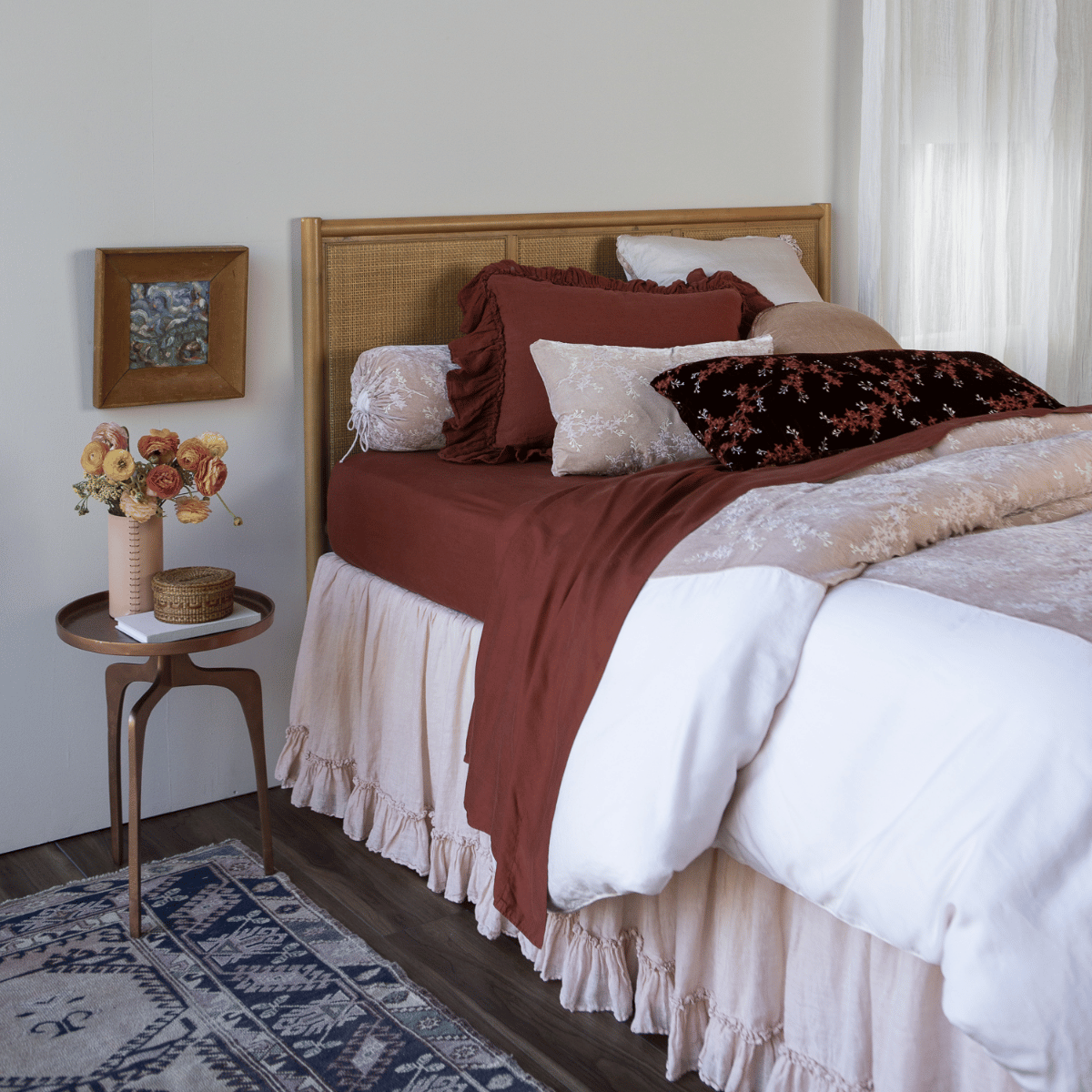 : a pale pink duvet cover with dark terrcotta colored sheets and pillows against a rattan headboard with coordinating side table - shot from a 3/4 angle.