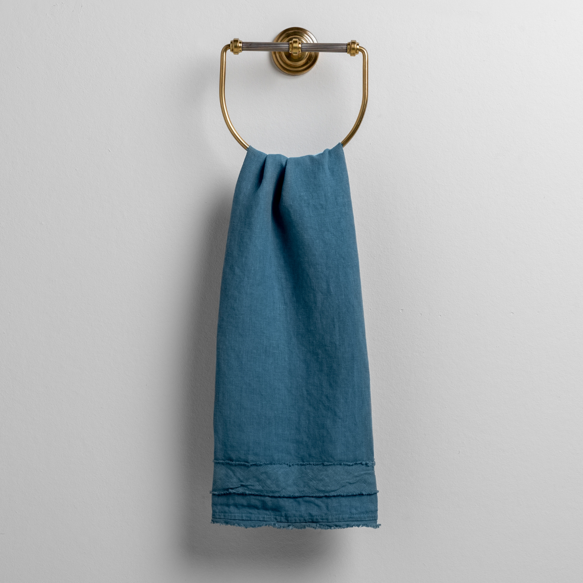 Cenote: midweight linen guest towel with raw edge band at both ends hanging from a towel ring mounted to a white wall.