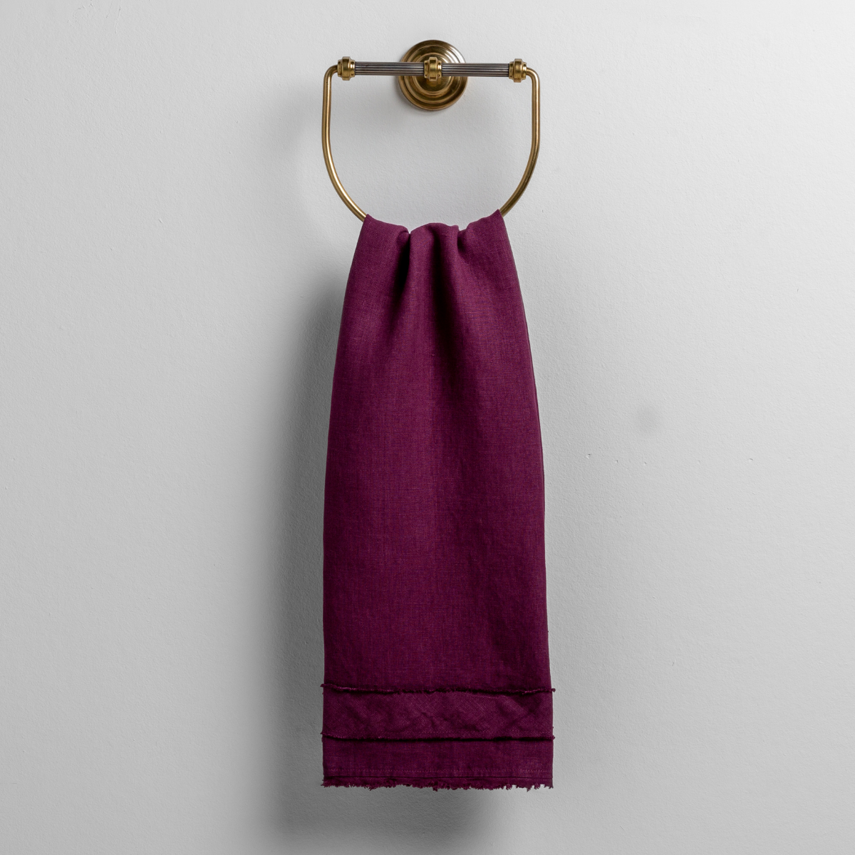 Fig: midweight linen guest towel with raw edge band at both ends hanging from a towel ring mounted to a white wall.