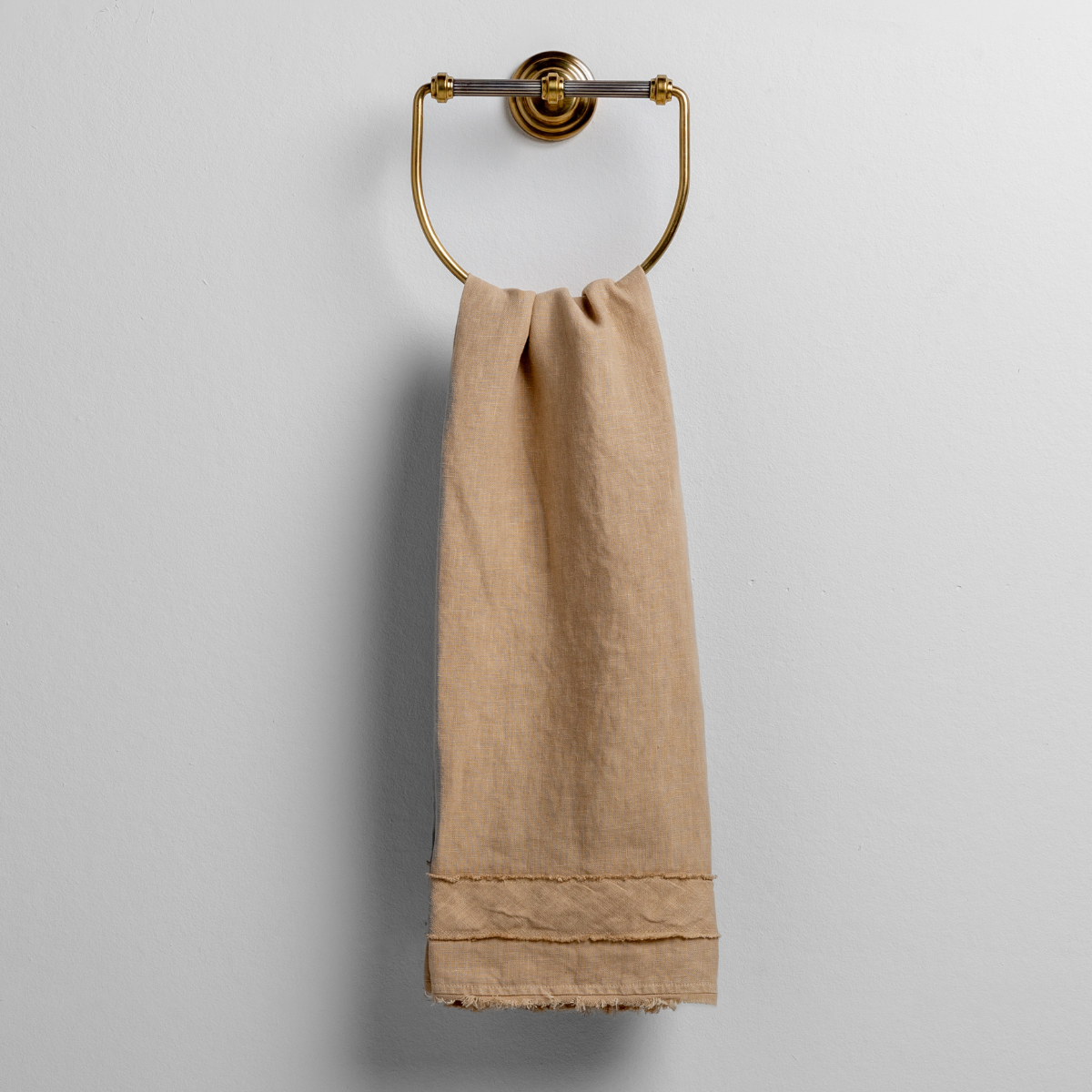 Honeycomb: midweight linen guest towel with raw edge band at both ends hanging from a towel ring mounted to a white wall.