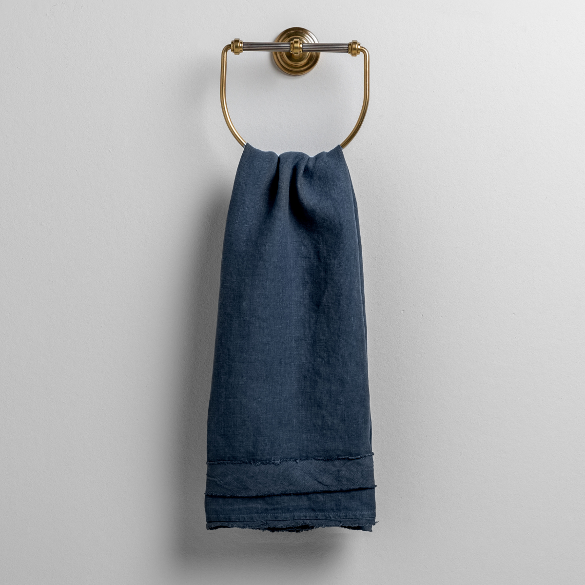 Midnight: midweight linen guest towel with raw edge band at both ends hanging from a towel ring mounted to a white wall.