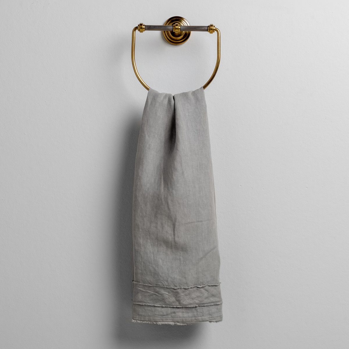 Mineral: midweight linen guest towel with raw edge band at both ends hanging from a towel ring mounted to a white wall.