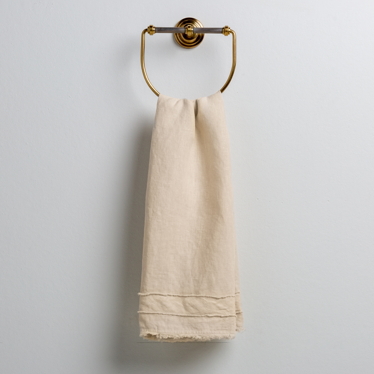 Parchment: midweight linen guest towel with raw edge band at both ends hanging from a towel ring mounted to a white wall.