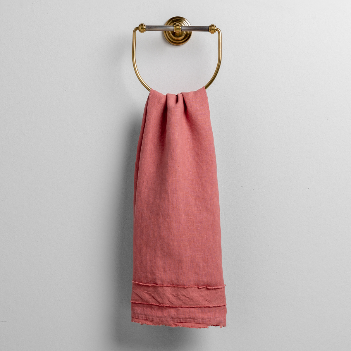 Poppy: midweight linen guest towel with raw edge band at both ends hanging from a towel ring mounted to a white wall.