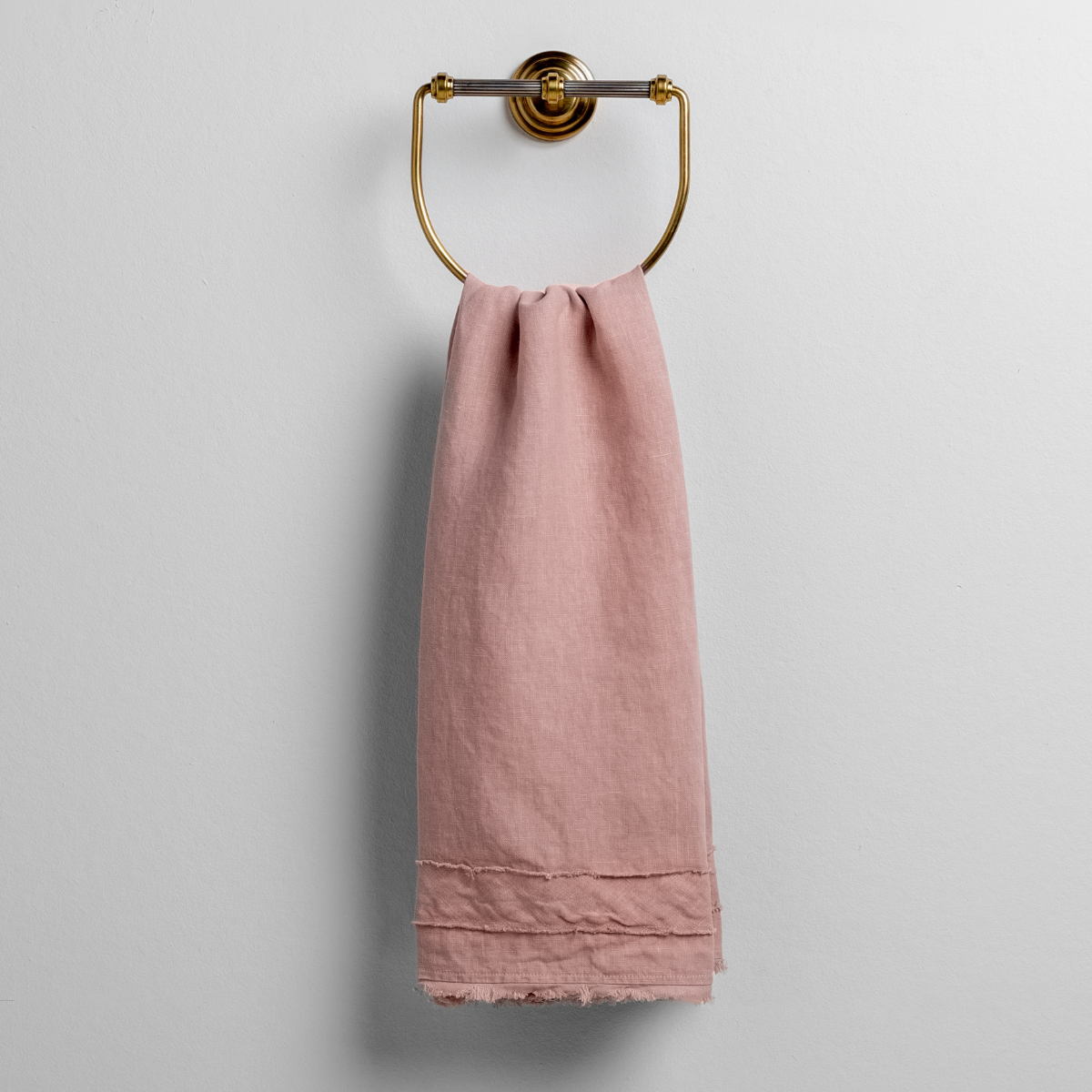 Rouge: midweight linen guest towel with raw edge band at both ends hanging from a towel ring mounted to a white wall.