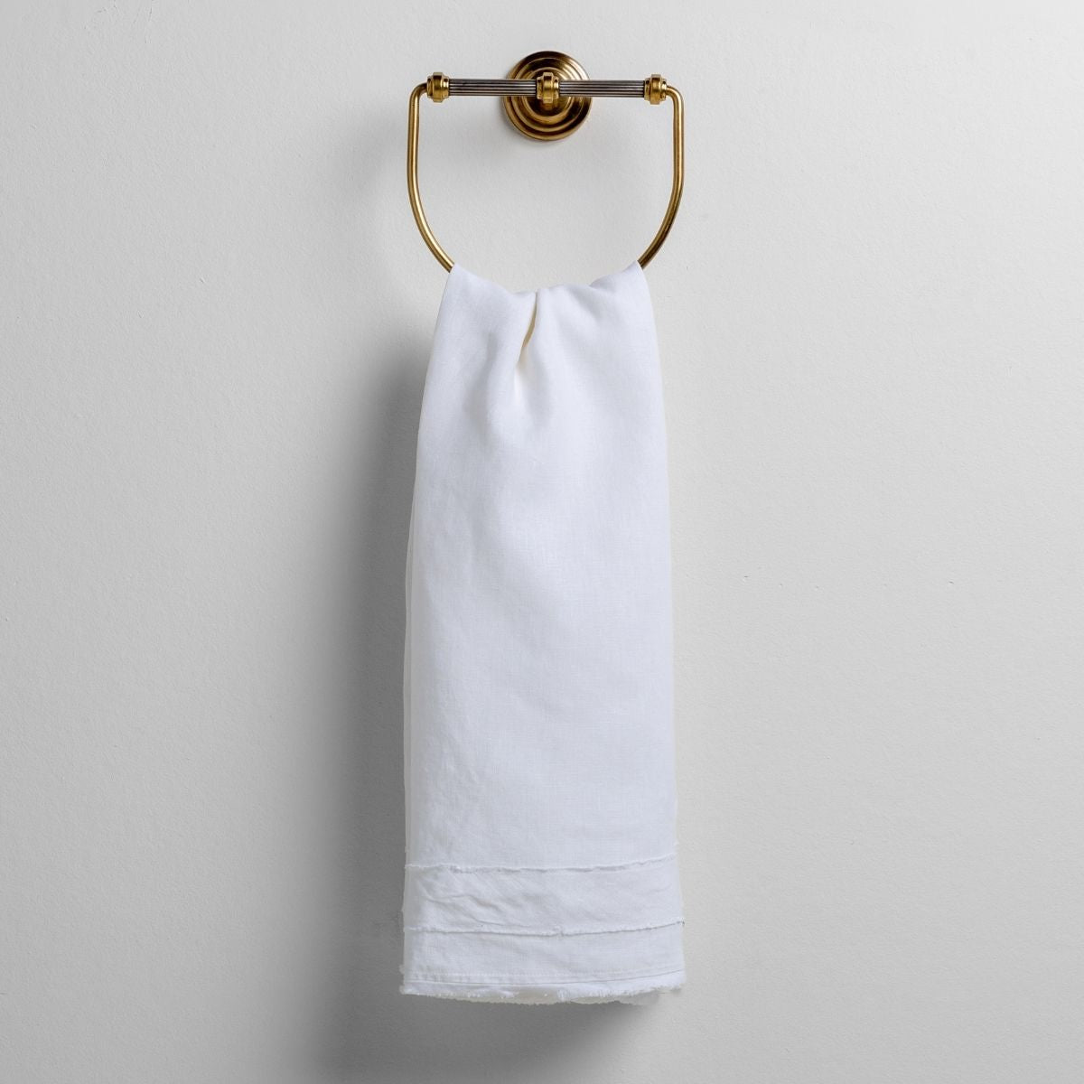 White: midweight linen guest towel with raw edge band at both ends hanging from a towel ring mounted to a white wall.