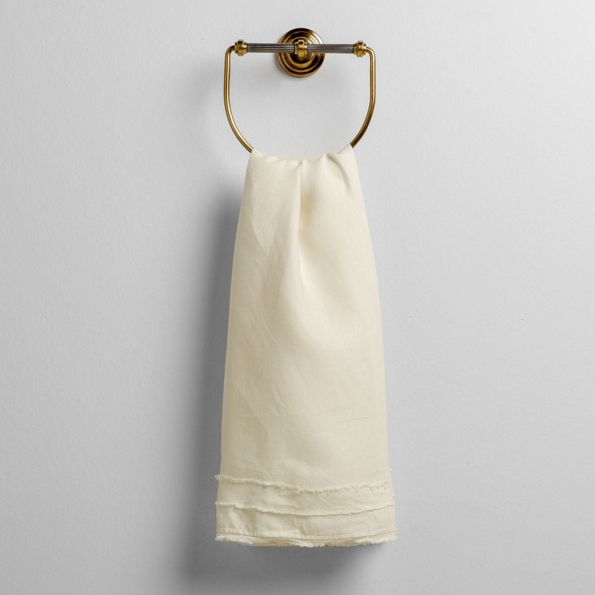 Winter White: midweight linen guest towel with raw edge band at both ends hanging from a towel ring mounted to a white wall.