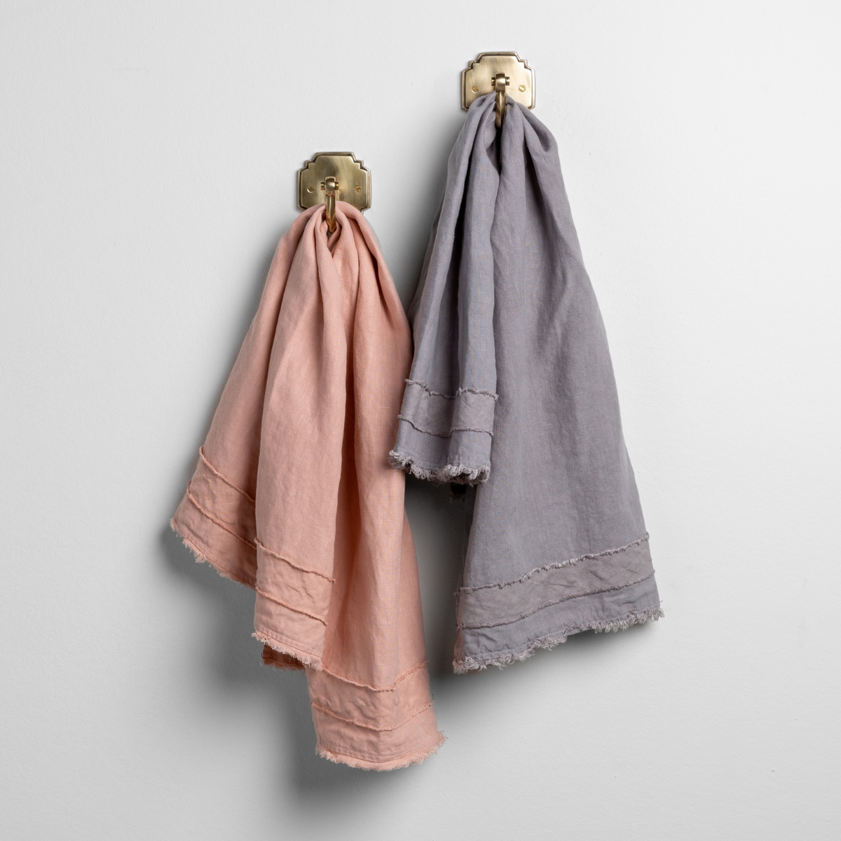 Rouge: pair of midweight linen guest towels in rouge and moonlight on gold towel hooks mounted to a white wall.