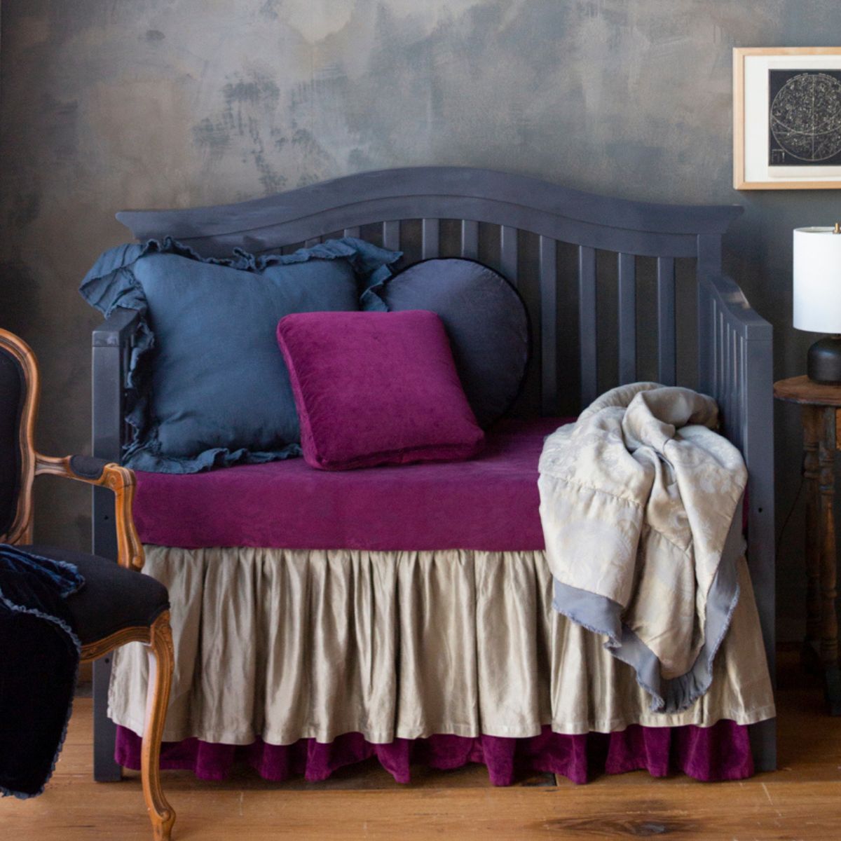 : a moody crib scene with jewel tones against a medium wood floor and limewashed wall.