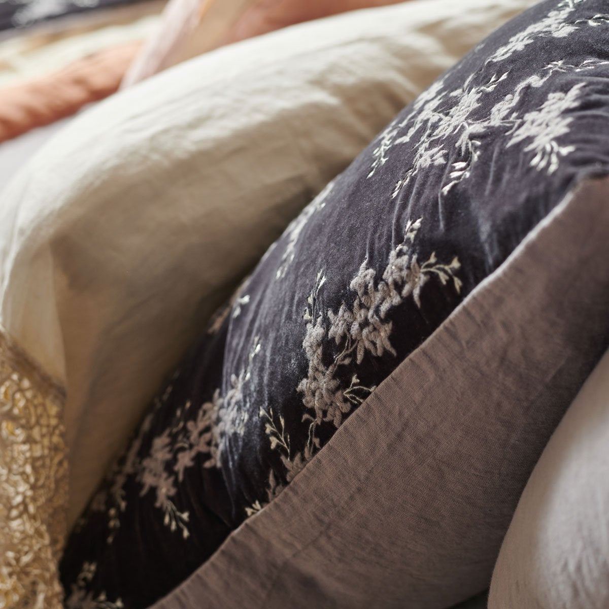 : Close-up of a Moonlight Lynette sham from the side layered behind a cream linen sleeping pillow showcases the subtler hue of the embroidery and the linen back.