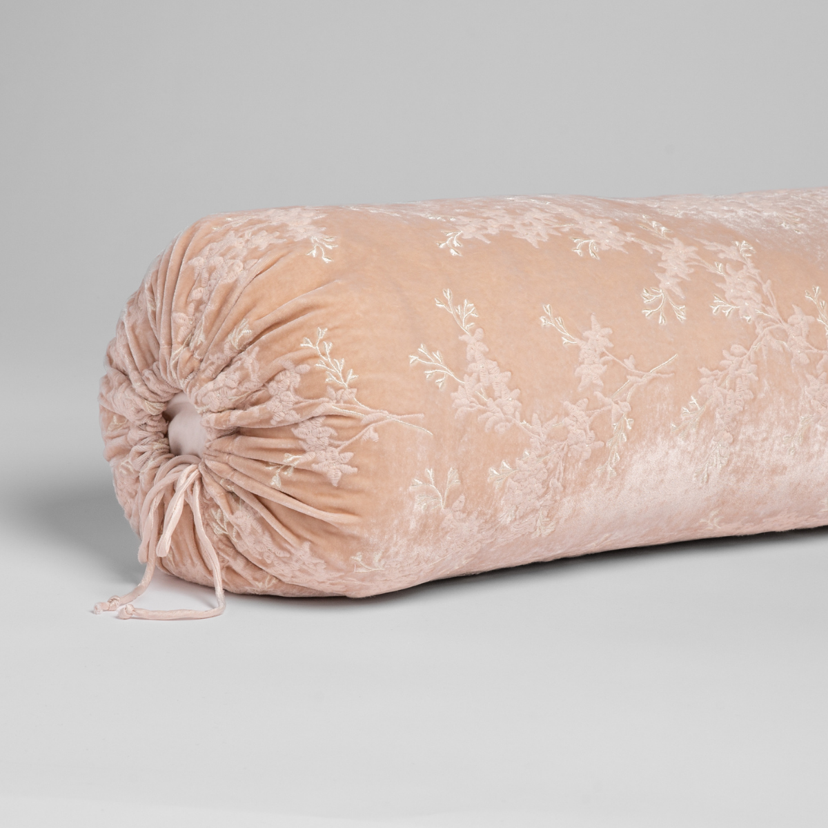 Pearl: A close-up of the cinched end of the embroidered silk velvet bolster pillow shown against a white background.