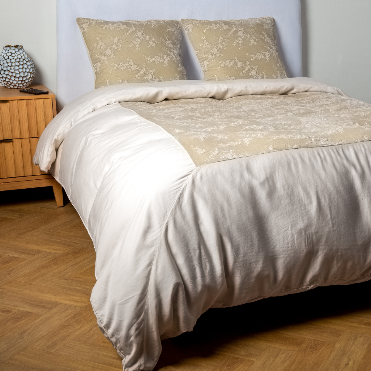Parchment: A ¾ angle shot of an embroidered silk velvet and tencel duvet cover and matching shams with a vase and cell phone on the side table.