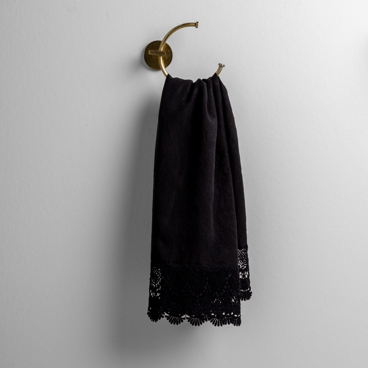 Corvino: linen with mattine lace trimmed guest towel on a decorative towel ring mounted on a white wall.