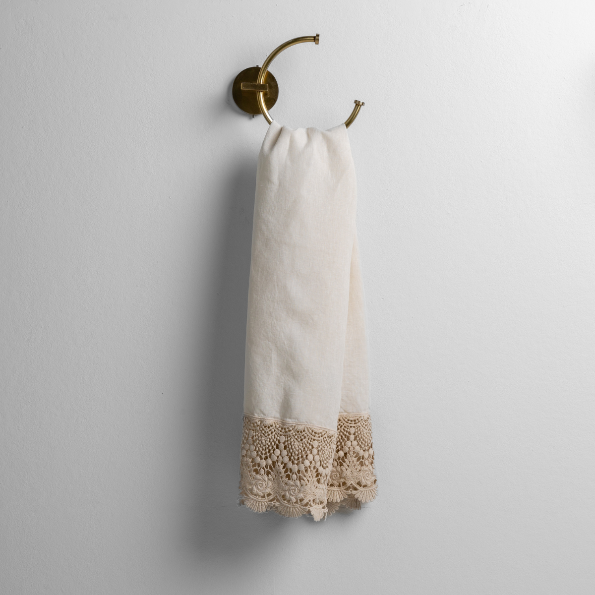 Parchment: linen with mattine lace trimmed guest towel on a decorative towel ring mounted on a white wall.
