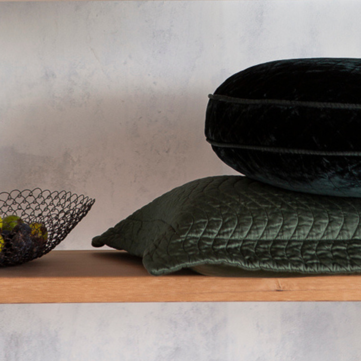 : quilted throw pillows in silk velvet and cotton sateen in juniper, a deep green on a shelf with a wire bowl.