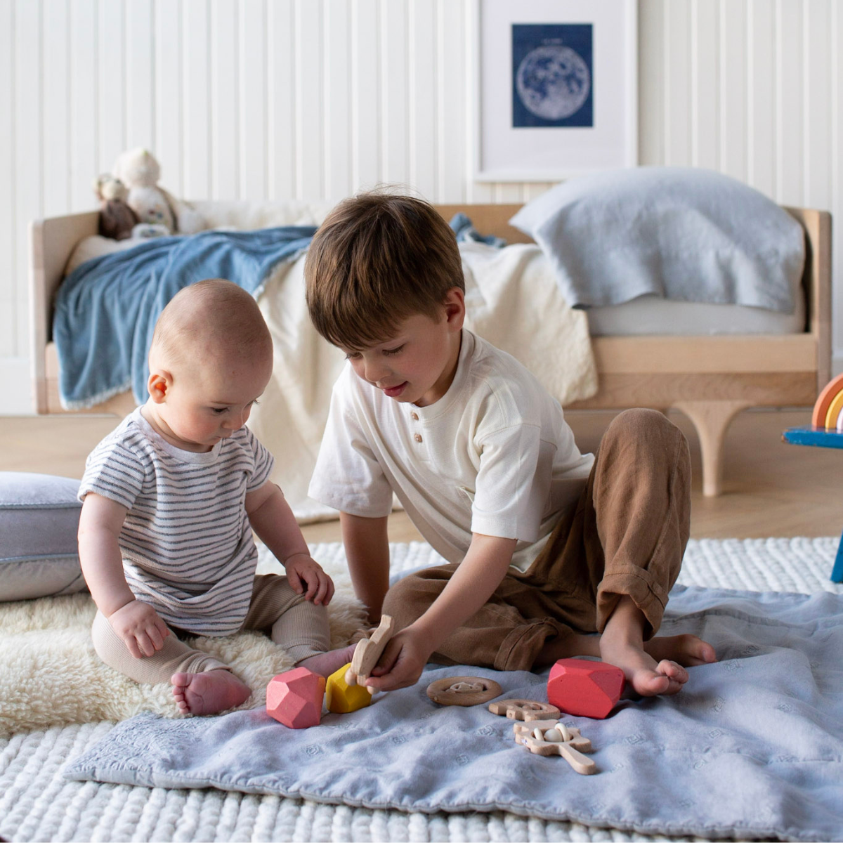 : Preschooler and baby sitting on blanket in cloud, playing with wooden blocks and teethers.