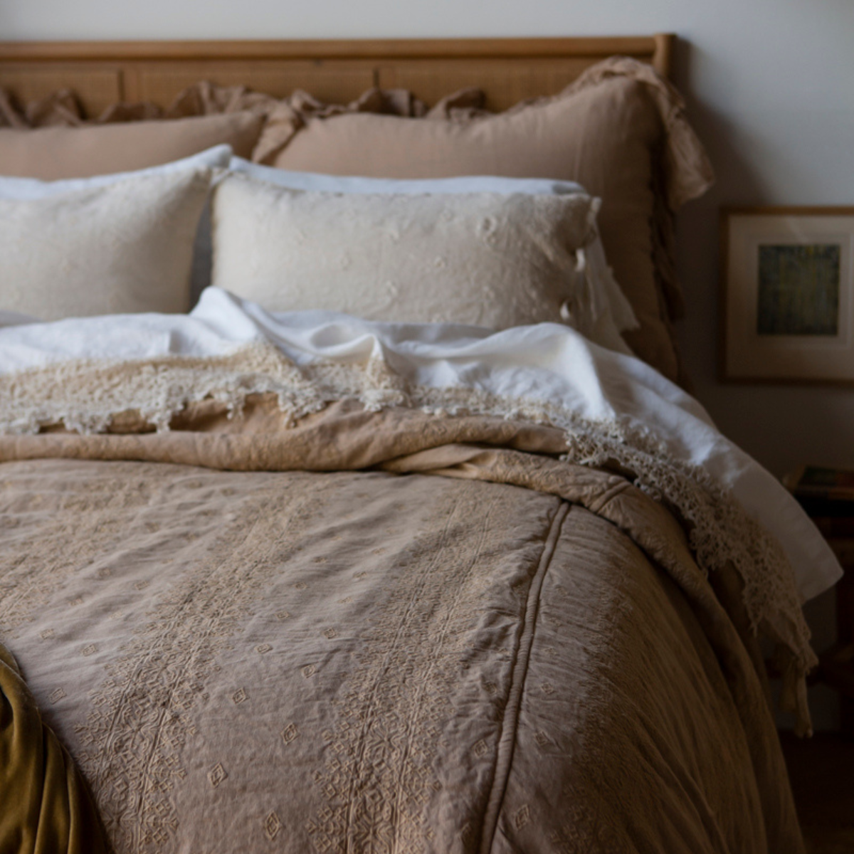 : The bedspread in honeycomb showcases the intricate embroidery in a neutral toned bedroom - partial end of bed view.