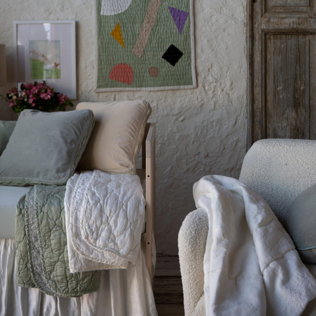 : Close up of blankets in winter white and eucalyptus, folded over the front of a crib in a tonal nursery scene.