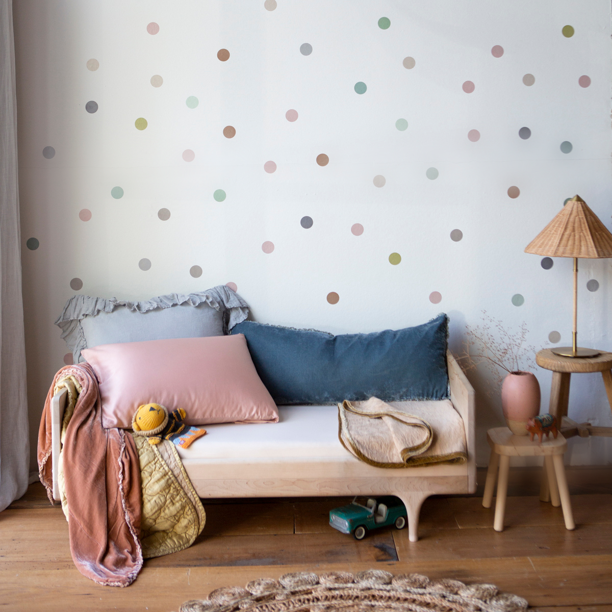 : Blanket in honeycomb folded on a wooden toddler bed, shown with pink, gold, and blue pillows and blankets in a bright and warm children's room.