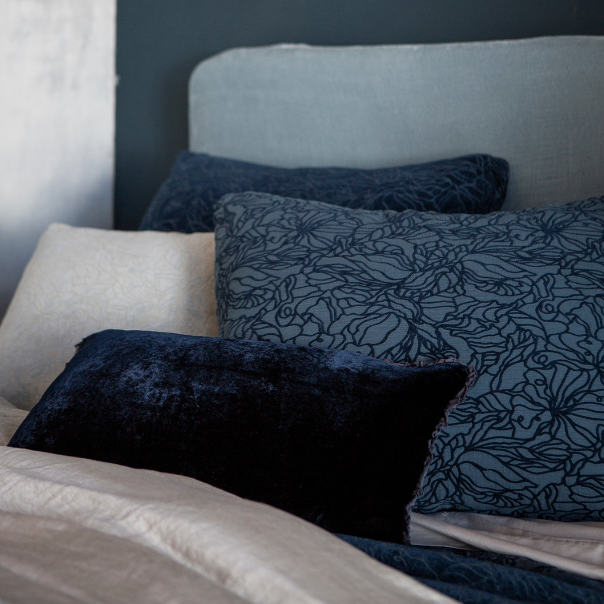 : shams and a throw pillow shown against a light blue headboard all in blue tones.
