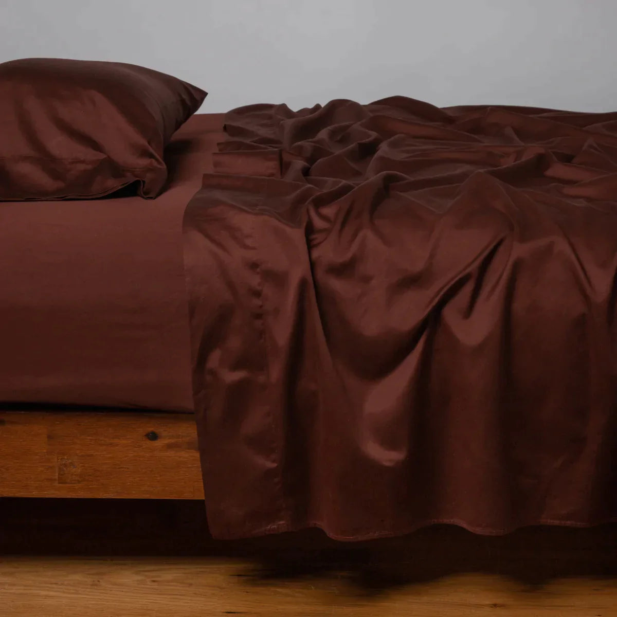 Mahogany: Cotton sateen flat sheet, shown with matching fitted sheet and sleeping pillow - side view.