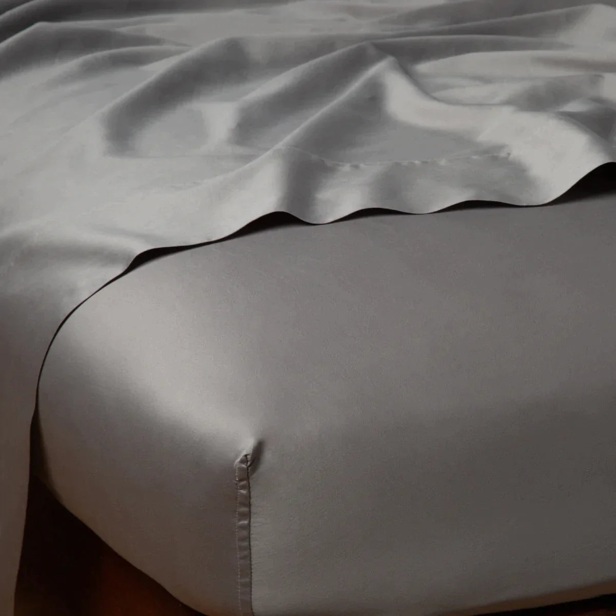 Moonlight: Cotton sateen flat sheet draped over matching fitted sheet. Shown from the top corner, the flat sheet is rumpled, highlighting the shine of the fabric.