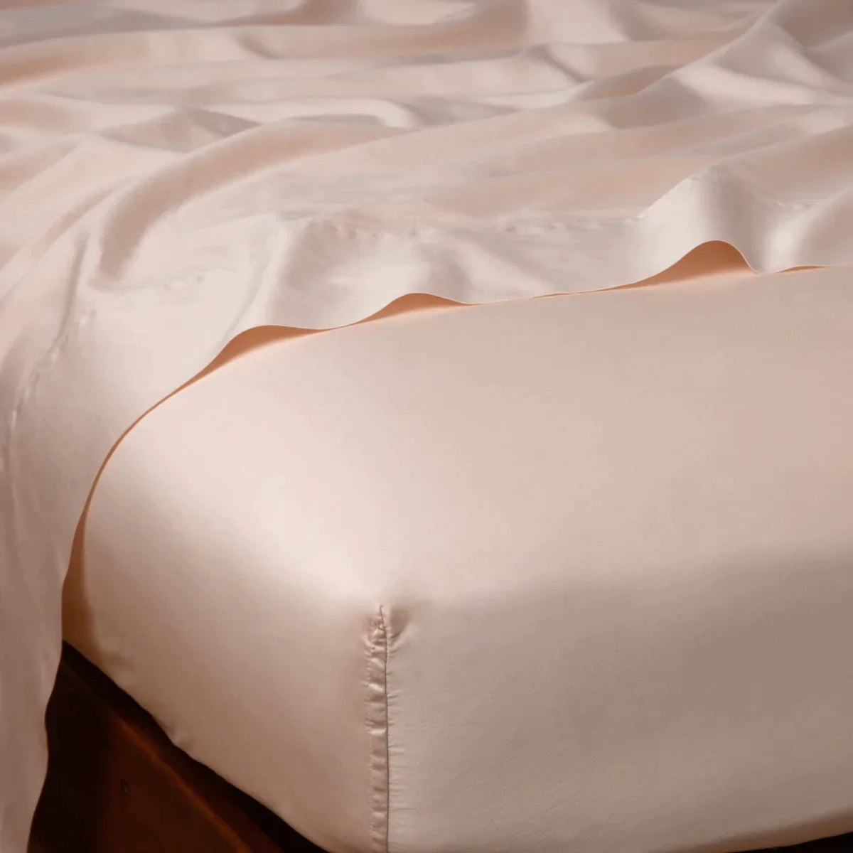 Pearl: Cotton sateen flat sheet draped over matching fitted sheet. Shown from the top corner, the flat sheet is rumpled, highlighting the shine of the fabric.