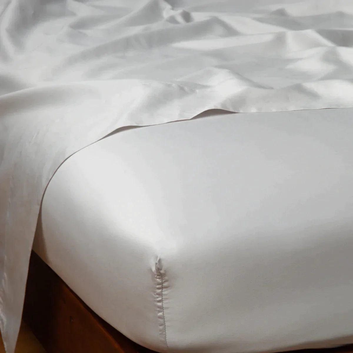 Sterling: Cotton sateen flat sheet draped over matching fitted sheet. Shown from the top corner, the flat sheet is rumpled, highlighting the shine of the fabric.