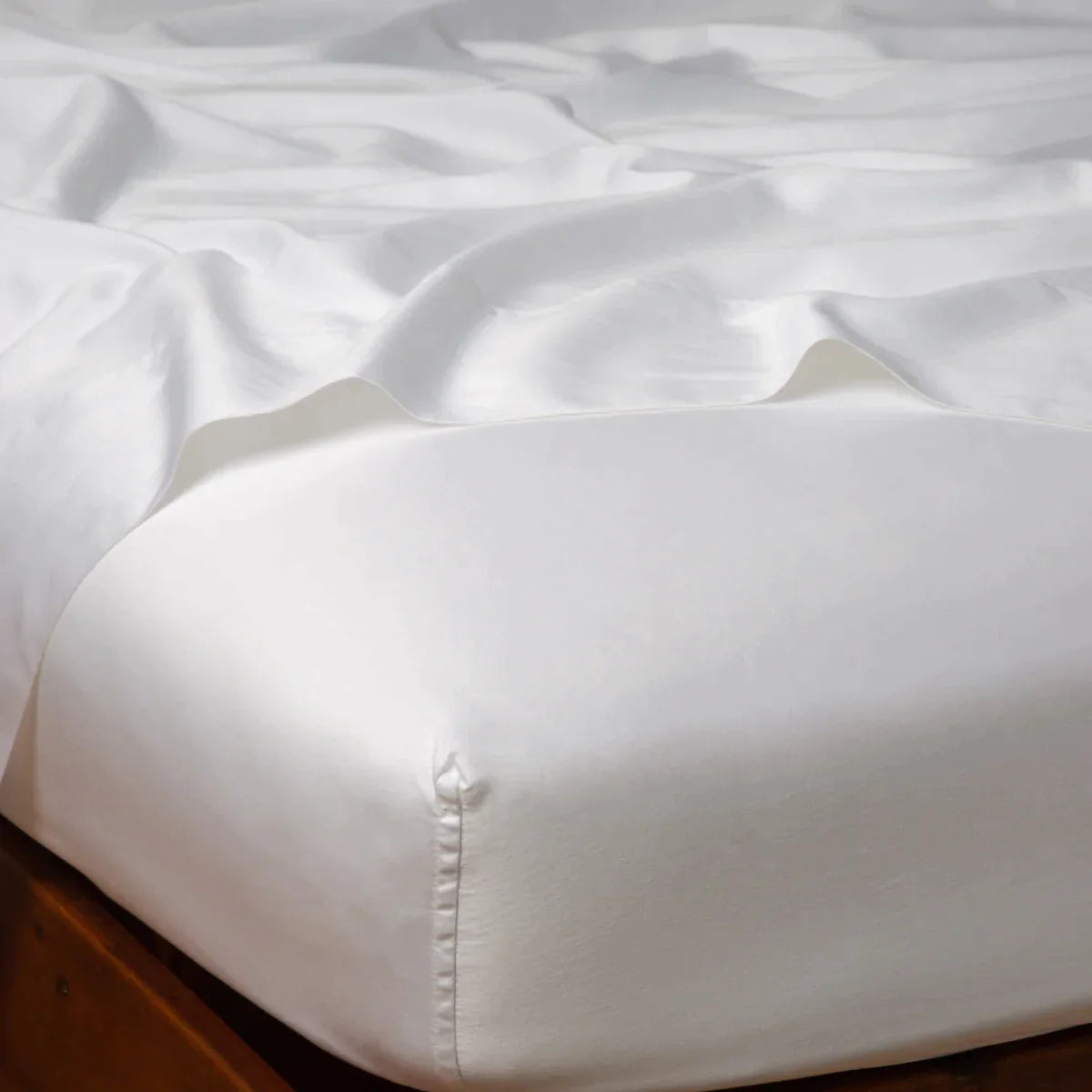 White: Cotton sateen flat sheet draped over matching fitted sheet. Shown from the top corner, the flat sheet is rumpled, highlighting the shine of the fabric.