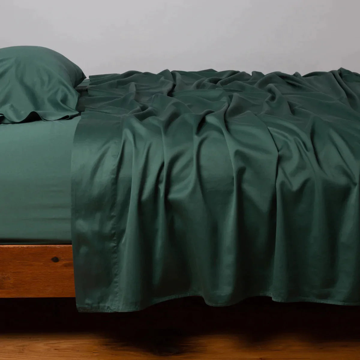 Jade: Cotton sateen sleeping pillow, on a bed with matching sheets - side view.