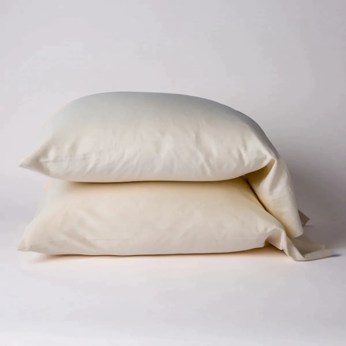 Parchment: Two cotton sateen sleeping pillows, stacked neatly against a white backdrop - side view.