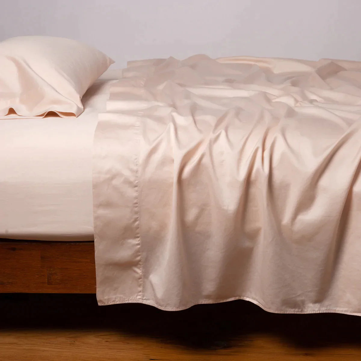 Pearl: Cotton sateen sleeping pillow, on a bed with matching sheets - side view.