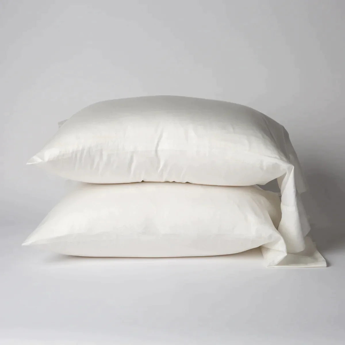 Winter White: Two cotton sateen sleeping pillows, stacked neatly against a white backdrop - side view.