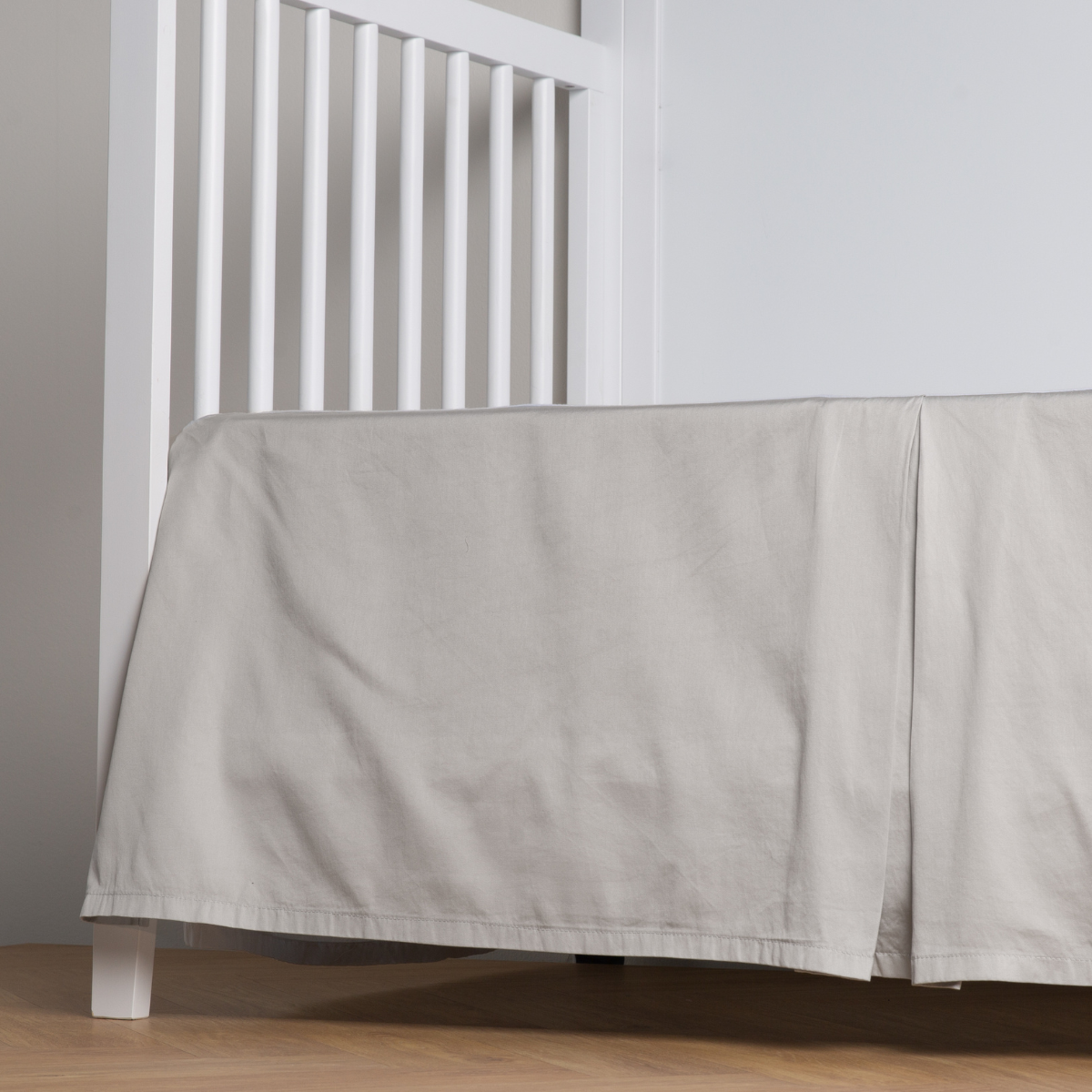 Cloud: cotton sateen cribi skirt with a center pleat shown straight on from a slight angle in a crib without a crib mattress.