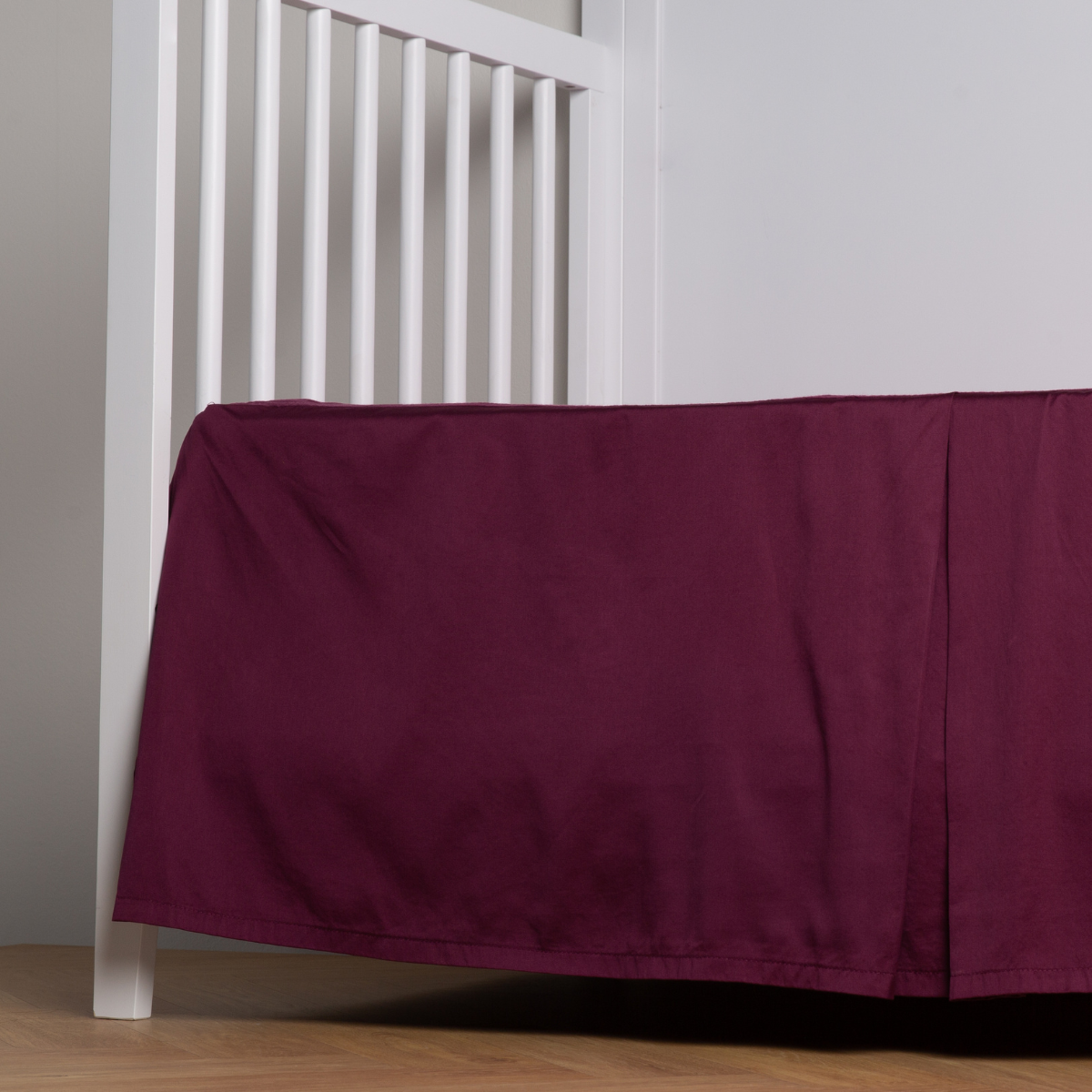 Fig: cotton sateen cribi skirt with a center pleat shown straight on from a slight angle in a crib without a crib mattress.