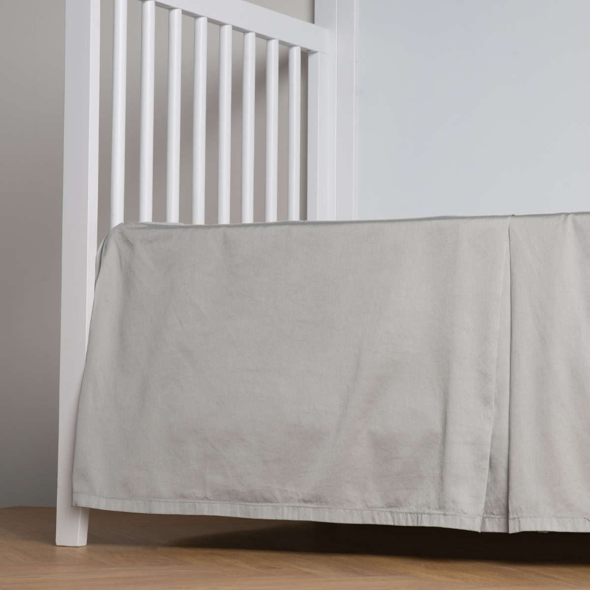 Mineral: cotton sateen cribi skirt with a center pleat shown straight on from a slight angle in a crib without a crib mattress.
