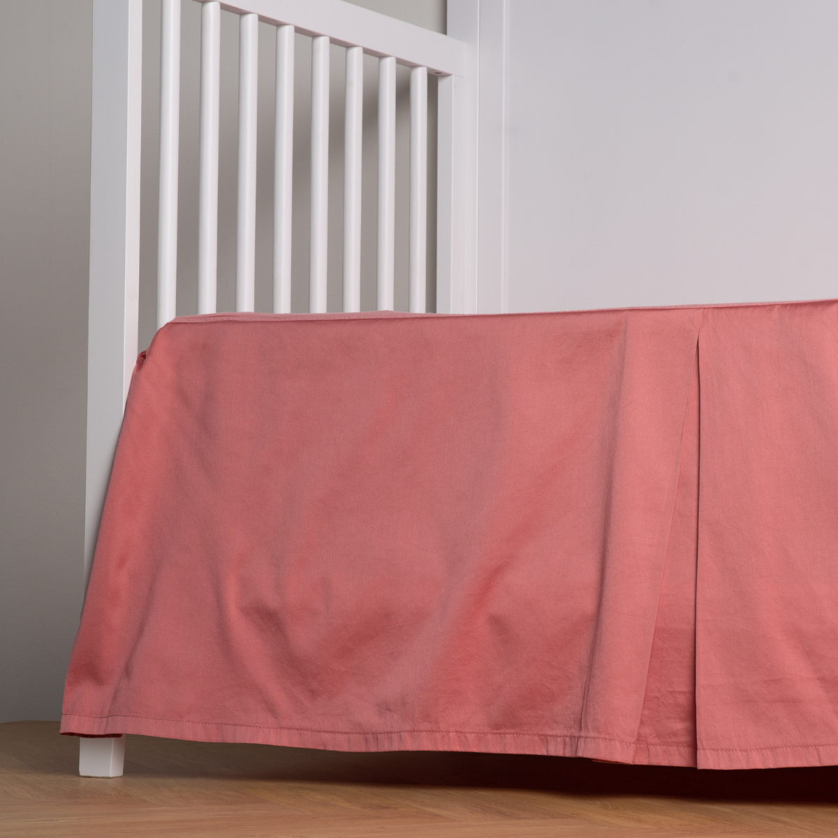 Poppy: cotton sateen cribi skirt with a center pleat shown straight on from a slight angle in a crib without a crib mattress.
