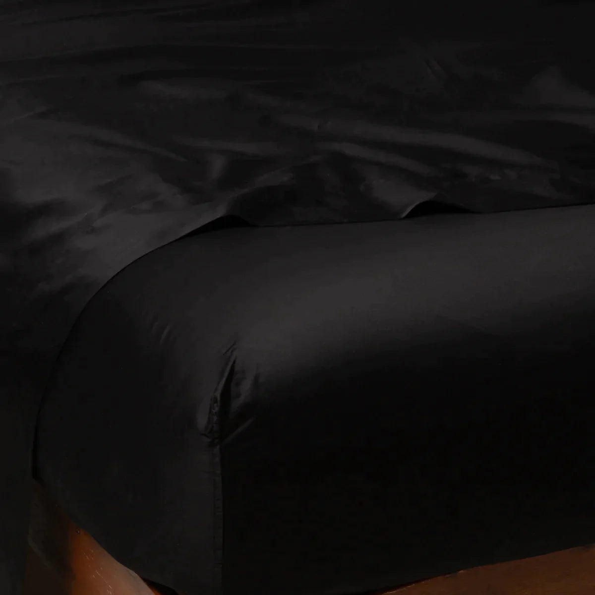Corvino: Cotton sateen flat sheet draped over matching fitted sheet. Shown from the top corner, the flat sheet is rumpled, highlighting the shine of the fabric.