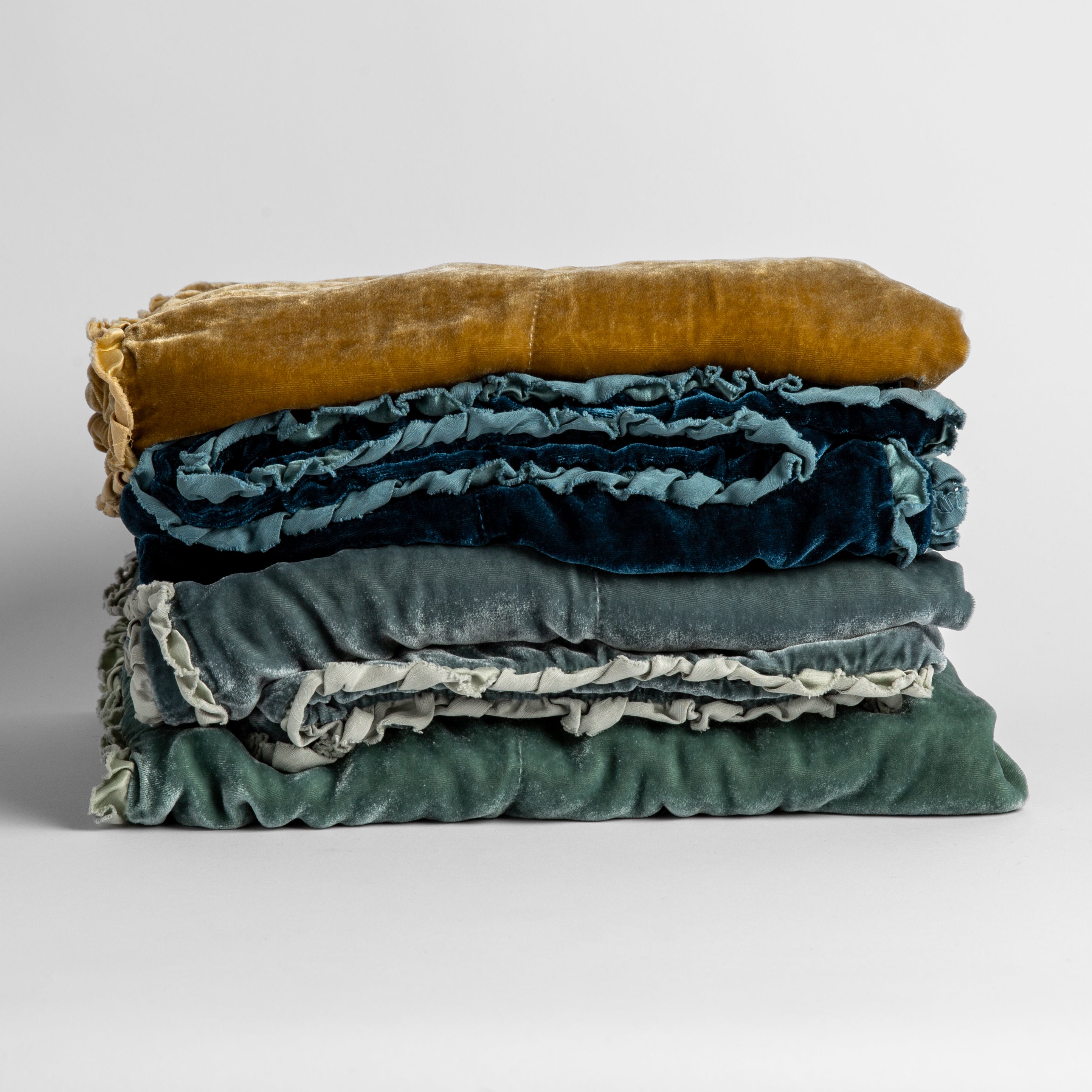 Stack of four silk velvet baby blankets with charmeuse trim shown against a white background. Blankets shown in Honeycomb, Cenote, Mineral and Eucalyptus.