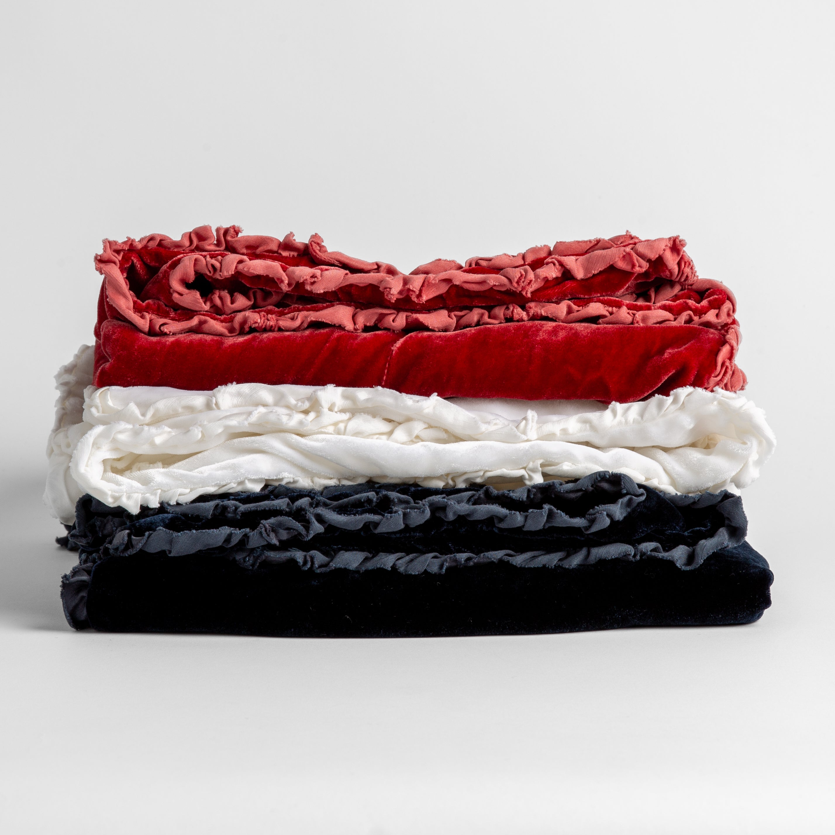 Stack of four silk velvet baby blankets with charmeuse trim shown against a white background. Blankets shown in Poppy, White and Midnight.
