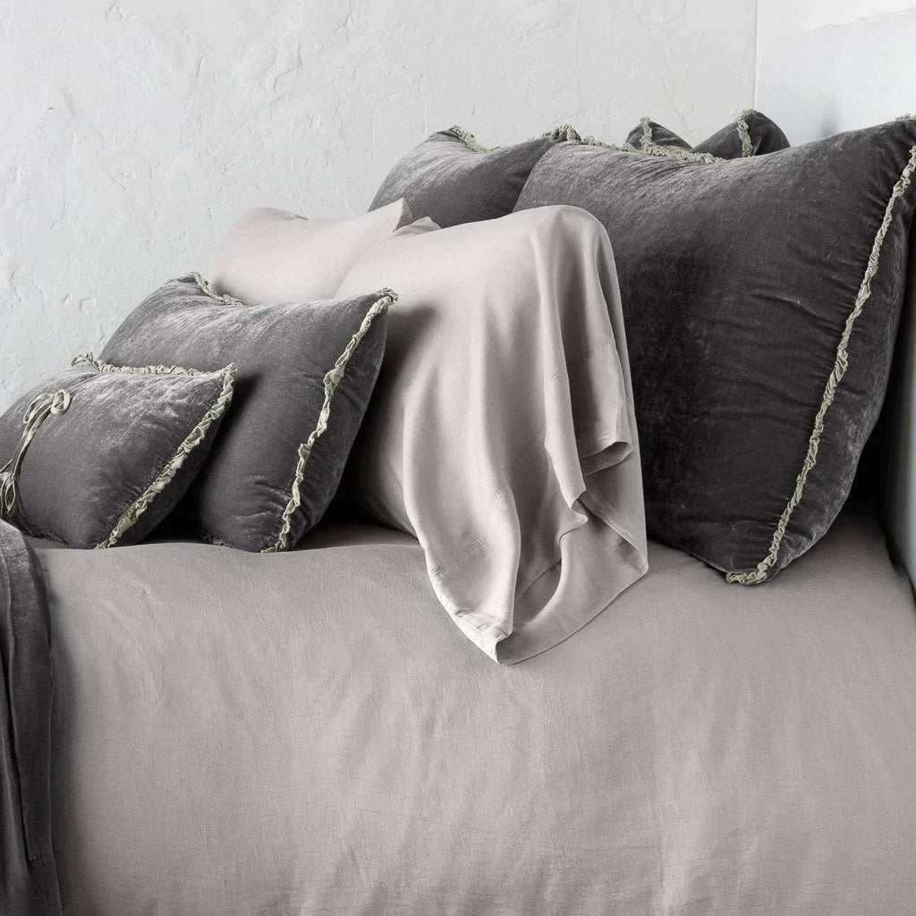 Fog: Silk velvet shams with a petite ruffle on monochromatic bed, leaning upright behind sleeping and throw pillows - side view.