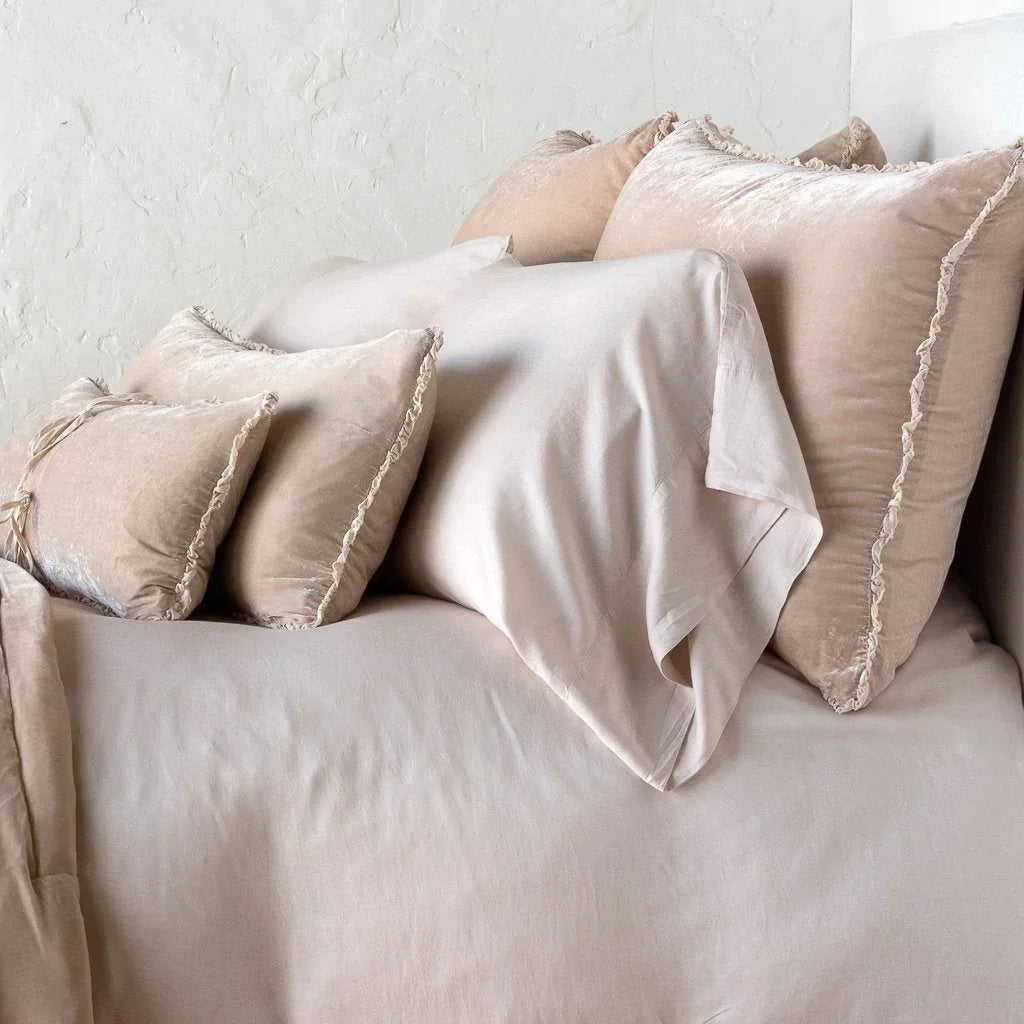 : Carmen shams in pearl on monochromatic bed, leaning upright behind sleeping and throw pillows. Close-up side view showcases the charmeuse petite raw-edge ruffle.