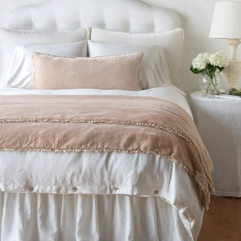 Pearl: Silk velvet shams with a petite ruffle on a white bed, stacked behind sleeping and throw pillows - view from end of bed.